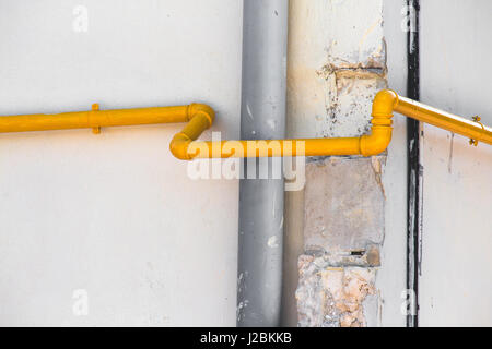 Wasser, Gas und Kanalisation Sanitär läuft auf der Außenseite eines Gebäudes. Gelbe, graue, schwarze Rohre. Natürlichen hellen, weißen Wand Hintergrund. Stockfoto