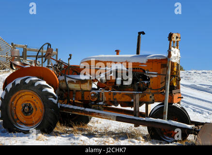Orange Traktor sitzt im Freien bei dem Wetter.  Schnee liegt auf Reifen und Kapuze.  Schneepflug ist beigefügt. Stockfoto