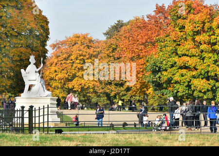 Kensington Gardens UK Royal Park Touristen & Besucher an die weiße Marmorstatue von Königin Victoria im Kensington Palace mit Herbstfarben der Bäume über Stockfoto