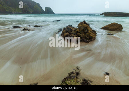 eine Welle von der steigenden Flut spült über den Strand und den Felsen unterhalb der Klippen von Camus Mor, Schottland Stockfoto