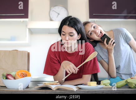 2 junge Frauen, die Spaß in der Küche Stockfoto