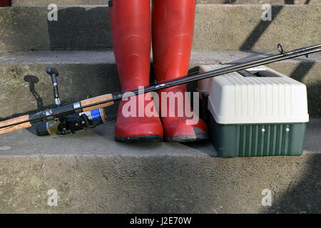 Angelrolle, rote Gummistiefel und Tackle Box auf Treppen. Stockfoto