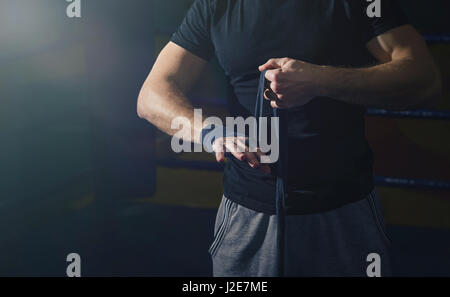 Nahaufnahme der Hand von einem jungen Boxer, der Boxen Bandagen windet sich vor einem Spiel, Kampf oder Training. Der Sonnenstrahl wird es in den dunklen Ring zu erleichtern. Stockfoto