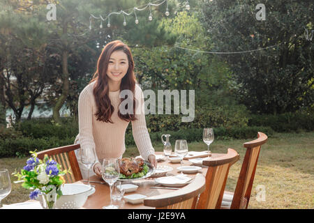 Junge lächelnde Frau, die er Essen auf Tisch im Garten Stockfoto