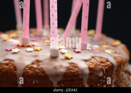 Nahaufnahme einer Feier Kuchen mit Zuckerguss, Hunderte und Tausende Dekoration und rosa Kerzen auf einem schwarzen Hintergrund Stockfoto