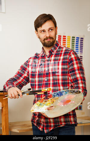 Mann-Künstler hält in seinen Händen, einen Pinsel und eine Holzpalette mit Ölfarben. Porträt. Stockfoto