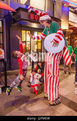 Ein üppiger junge springt hoch fünf einen Clown auf Stelzen an ein Weihnachtsfest in einem Einkaufszentrum in Costa Mesa, CA. Hinweis: Mutter und Tochter. Stockfoto