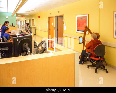 Eine ältere Frau Musiker spielt die Harfe auf dem Flur eines Krankenhauses Irvine, CA, um den Patienten zu beruhigen. Hinweis Pflegestation. Stockfoto