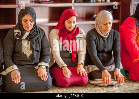 In einem separaten Raum ein Hijabs oder Kopftücher tragen, Knien muslimische Frauen in Abrahamitische Gebet während der Predigt oder Khutbah während der Gottesdienste in einer Moschee in Anaheim, CA. Beachten Sie die traditionellen orientalischen Kleidung. Stockfoto