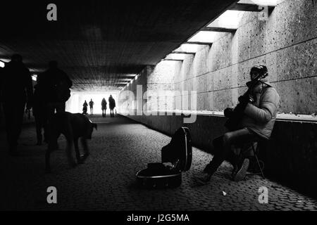 Straße Straßenmusiker / Musiker spielt eine Gitarre für Geld in einer Fußgängerunterführung in München, in der Nähe des englischen Gartens. Komposition in schwarz und weiß. 5 t Stockfoto