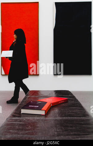 München, 5. Februar 2017.  Eine Frau der Asiate geht Vergangenheit einige Bücher angelegt auf einer Bank mit farblich Kunstwerk im Hintergrund. Mod Stockfoto