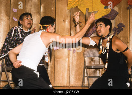 Athapaskische Mutter singt überliefert Lieder, während ihre beiden Söhne traditionelle Spiele während einer Versammlung in Alaska Native Heritage Center, Anchorage, AK zeigen Stockfoto