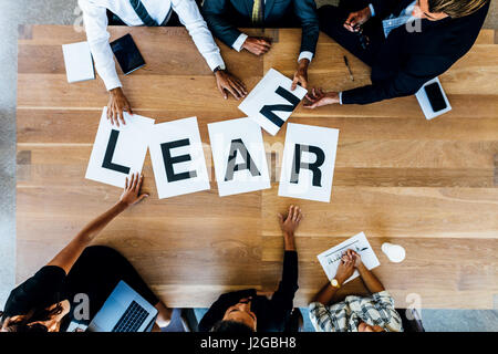 Gruppe von Menschen setzen Zeichen mit Alphabeten bilden das Wort lernen am Tisch. Geschäftsleute diskutieren über lernen in einer Besprechung. Stockfoto