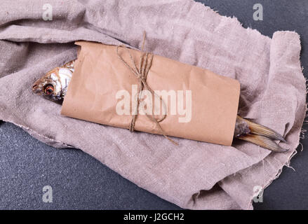 getrocknete Fische Roach eingewickelt in braunen Kraftpapier auf eine schwarze Fläche Stockfoto