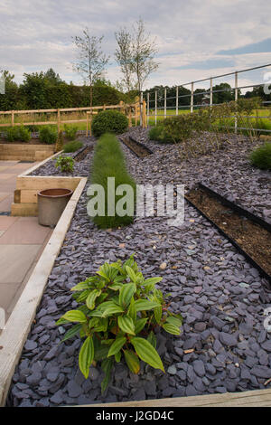 Schönen, gepflegten, privaten Garten mit modernem Design, gepflasterte Terrasse, Sträucher & Gräser in Linien auf erhöhte Grenze - Yorkshire, England, UK. Stockfoto