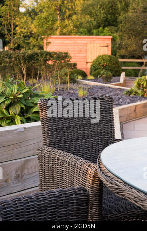 Private, zeitgenössisch gestalteten, Garten, England, UK - Nahaufnahme des Stuhls im Sitzbereich (Patio-Möbel) ausgelöst Border, Sträucher & Schuppen jenseits. Stockfoto