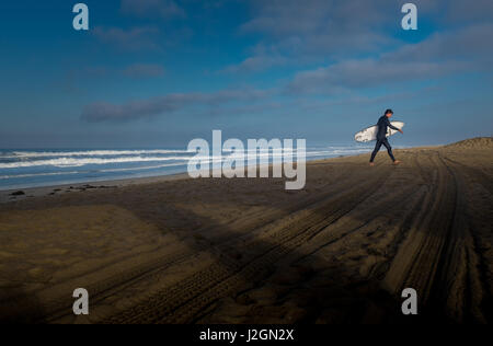 Ein einsamer Surfer am Strand kurz nach Sonnenaufgang am Huntington Beach, Kalifornien Stockfoto