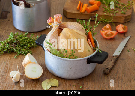 Rohem Hühnerfleisch in einem Kochtopf mit Zwiebel, Knoblauch, Karotten, Tomaten, Rosmarin, Lorbeer und Oregano. Stockfoto