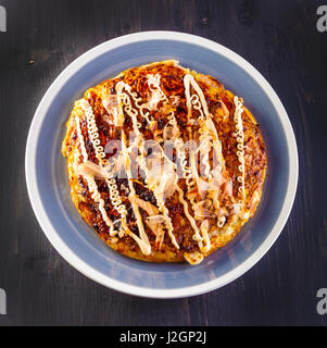 Japanisches Okonomiyaki auf einem schwarzen Holztisch. Ansicht von oben. Stockfoto