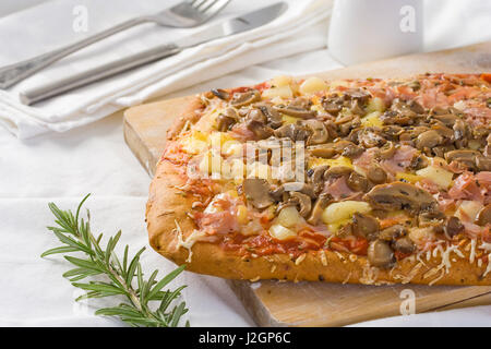 Pizza mit Tomaten, Käse, Schinken, Pilze und Ananas auf ein Schneidebrett. Stockfoto