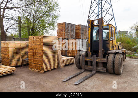 Große Gabelstapler und Stapel von neuen Holzbrettern und Nieten an den Holzplatz. Holzplatten auf Pfählen für Möbel-Materialien Stockfoto