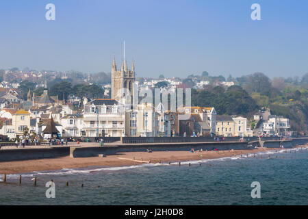 Blick auf Meer Teignmouth an einem sonnigen Frühlingstag mit Menschen zu Fuß entlang der Promenade. St. Michaels-Kirche steht im Vordergrund, im Hintergrund. Stockfoto