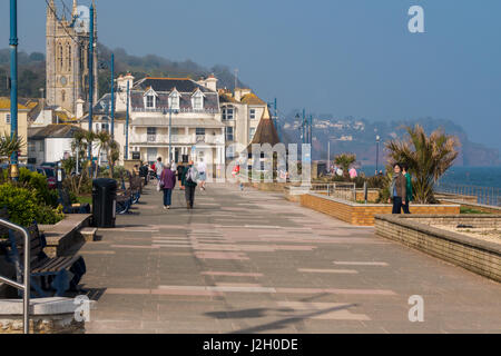 Blick auf Meer Teignmouth an einem sonnigen Frühlingstag mit Menschen zu Fuß entlang der Promenade. St. Michaels-Kirche steht im Vordergrund, im Hintergrund. Stockfoto