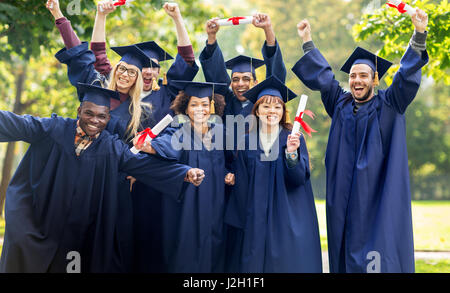 glückliche Schüler in Mörtel-Boards mit Diplomen Stockfoto