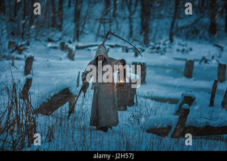 Schnee auf dem Feld ist der Mann mit der Sense des Todes. Er ist in einem Kapuzenpullover gekleidet und Schrecken verursacht. Stockfoto