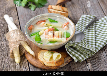 Spargel Suppe mit gebratenen Garnelen und Zuckerschoten, serviert mit geröstetem Baguette mit Butter rollt Stockfoto