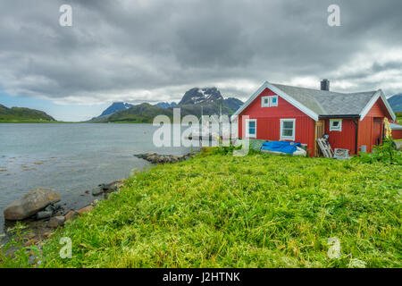 Einsames rotes Haus in diesem Fischerdorf befindet sich am Rand der Bucht, mit Blick auf hohe Küstengebirge, während eine Sturm nähert. Lofoten Stockfoto