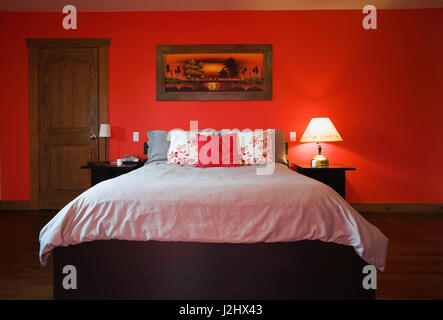 Queensize-bett auf Holzrahmen und Nachttische in hellen rot bemalten Wand im Schlafzimmer im skandinavischen Landhausstil Home anmelden. Stockfoto