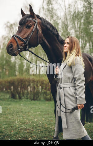 Schönes Mädchen kommuniziert mit dem Pferd im Park. Vorbereitung auf das Reiten Stockfoto