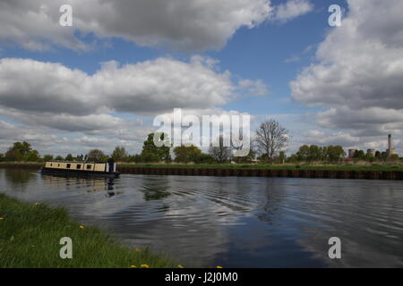 ein Lastkahn macht seinen Weg kontinuierlich entlang einer ruhigen Aire Calder Navigation Canal mit Reflexionen von Himmel, Wolken und Bäume auf dem Wasserweg Stockfoto