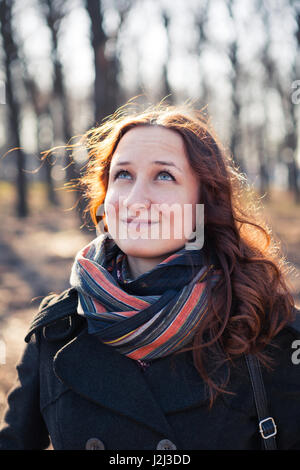 Lächelnde rothaarige Mädchen im Freien, weared Mantel und Schal. Vorfrühling im Park Ar Sonnenuntergang. Stockfoto