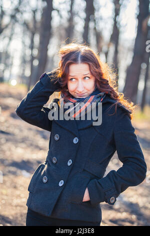 Lächelnde rothaarige Mädchen im Freien, weared Mantel und Schal. Vorfrühling im Park Ar Sonnenuntergang. Stockfoto