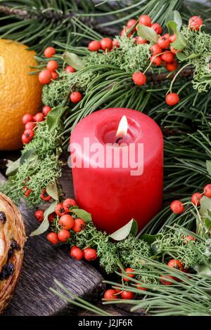 Rote Weihnachtskerze mit Moos und rote Beeren (Zwergmispel Horizontalis) Kranz geschmückt. Stockfoto