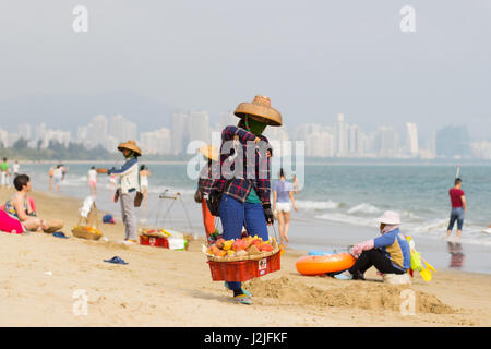 Sanya, China trägt 23. April 2017 - eine Frau-Verkäufer auf den Schultern eine Bar mit Körben voller Obst entlang des Strandes das Südchinesische Meer in Sanya Stockfoto