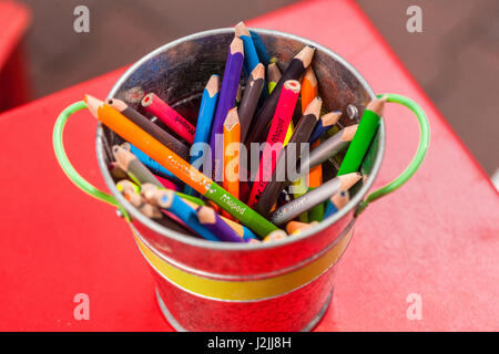 Bunte Bleistifte im Topf, Eimer auf rotem Tisch Stockfoto