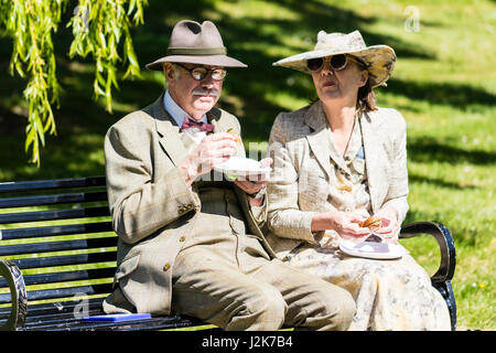 Gruß an die 40s Ereignis. Ein älteres Paar auf einer Parkbank ihre Sandwiches Pause für ein Foto zu posieren. Beide gekleidet in ca. 1940 Kostüm. Stockfoto