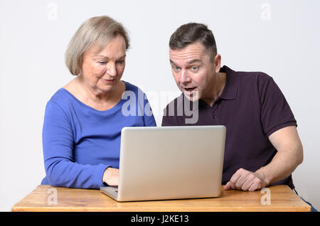 Begeisterte reifer Mann Blick auf Laptop mit senior Frau im blauen Hemd am Holztisch sitzen Stockfoto