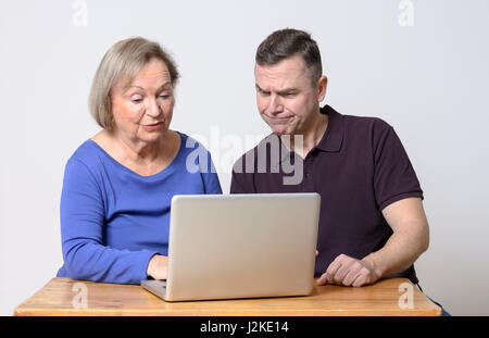 Mann mit verwirrten Ausdruck und lächelnde Frau in blauem Hemd mit Laptop-Computer über Holztisch Stockfoto