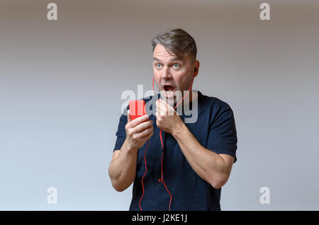 Mann mittleren Alters stehen isoliert in Schock und Horror mit großen Augen und sein Mund Agape, nachschlagen, auf grau mit Textfreiraum Stockfoto