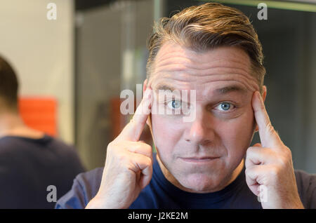 Kaukasischer Mann mittlerer Alter hält Finger zum Tempel und starrt auf die Kamera, während Sie im Bad stehen Stockfoto
