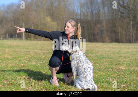 Hübsche junge Frau, die Lehre ihren Hund Befehle kniete in einem Feld neben ihr mit der Hand auf der Seite zeigen, wie das Tier Problemfälle in t aussieht Stockfoto