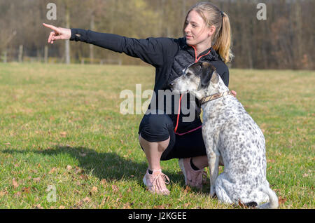 Hübsche junge Frau, die Lehre ihren Hund Befehle kniete in einem Feld neben ihr mit der Hand auf der Seite zeigen, wie das Tier Problemfälle in t aussieht Stockfoto