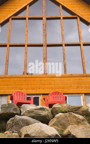 Red Adirondack Stühlen und Panoramafenstern an der hinteren Außenwand aus geschliffenem Eastern white pine Cottage Stil Hütte im Spätsommer anmelden. Stockfoto