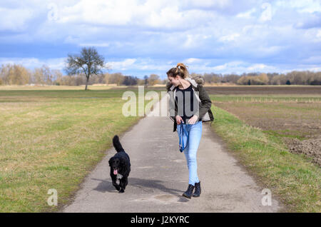 Junge sportliche Schülerin einen Lauf mit ihrem schwarzen Hund entlang der Landstraße durch Ackerland und Wiesen genießen, wie sie nebeneinander entlang joggen Stockfoto