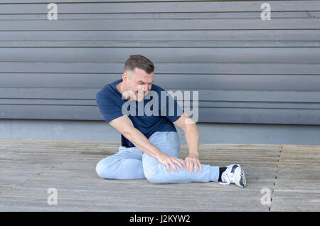 Sportlicher Mann mittleren Alters mit Muskelkrämpfen in seinem Kalb auf dem Boden umklammerte sein Bein und verzog das Gesicht vor Schmerzen Stockfoto