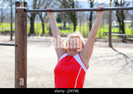 Beautiful senior Woman arbeiten auf einer horizontalen Leiste in einer ländlichen Sportarena in ein Fitness und gesunde Lebensweise-Konzept Stockfoto